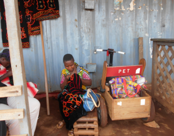 Nina devant sa boutique, brodant une robe pour une cliente, tous droits à Cameroon Baptist Convention Health Services, Cameroun